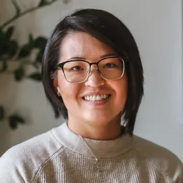 A smiling woman with glasses in a cozy indoor setting.
