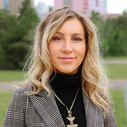 A woman in a patterned blazer standing outdoors in a black turtleneck.