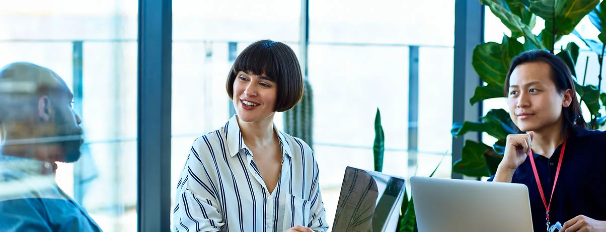 Three professionals discussing in a modern workspace with plants.