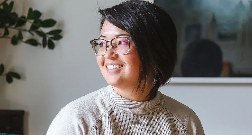 Smiling woman with short hair and glasses in a cozy setting.