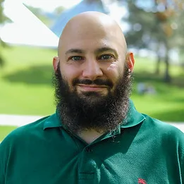 Smiling man in a green polo shirt outdoors.