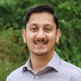 A smiling man in a light gray shirt with a green background.