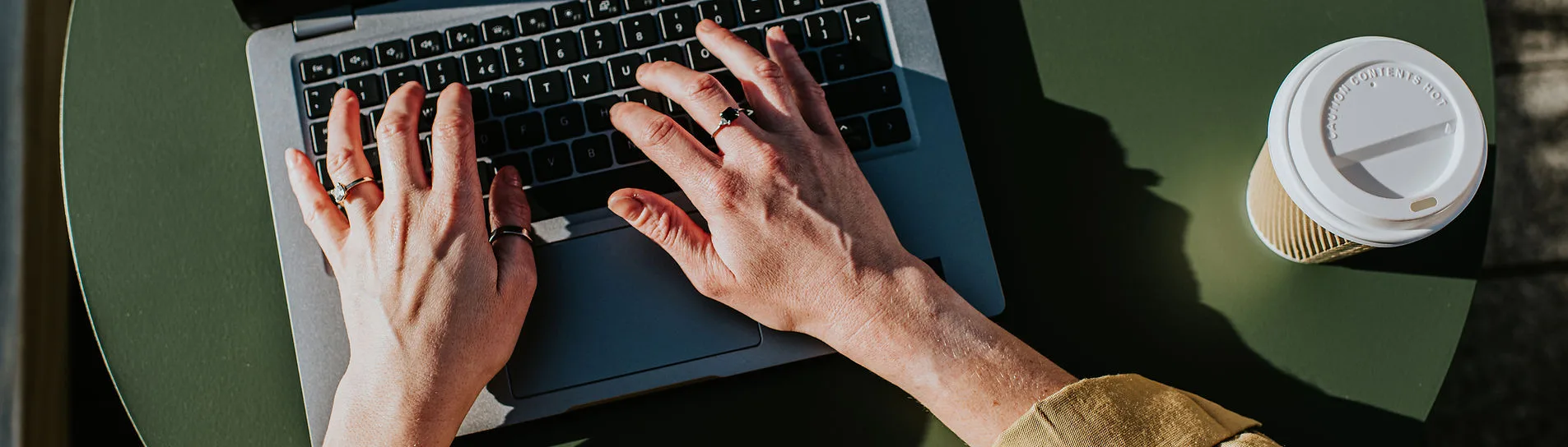 Hands typing on a laptop with a coffee cup nearby.