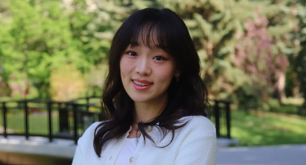 A young woman smiling in a park setting.