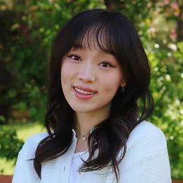 A young woman smiling in a green outdoor setting.