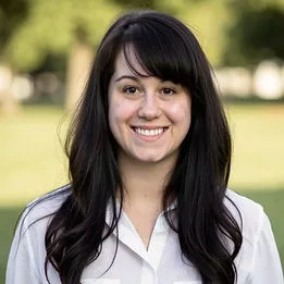 A smiling woman with long dark hair outside.