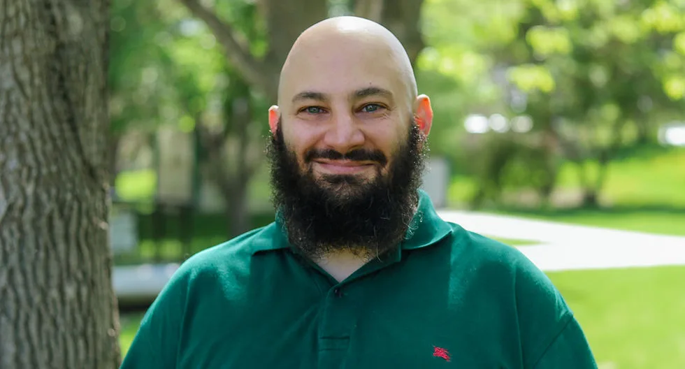 A smiling man with a beard in a green polo shirt outdoors.