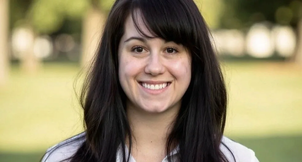 Smiling woman with long dark hair in a park.