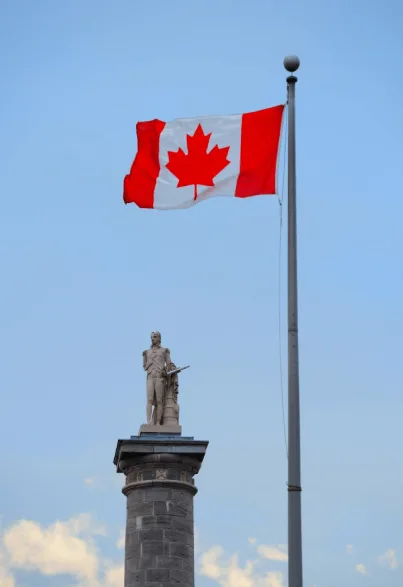 Canadian flag on a pole with a soldier statue below.