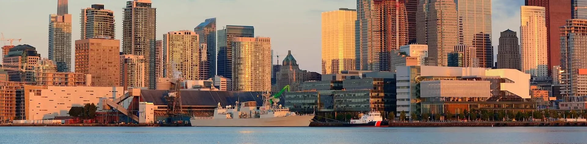 Urban skyline with buildings and ships during sunset.