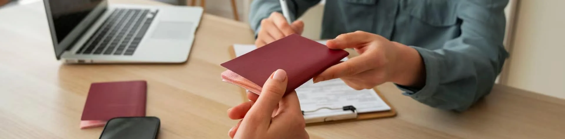 Hands exchanging a maroon passport in an office setting.