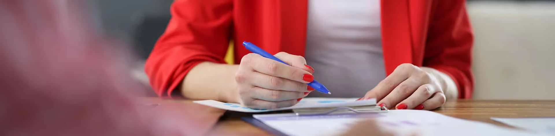 A person writing on a document with a blue pen.