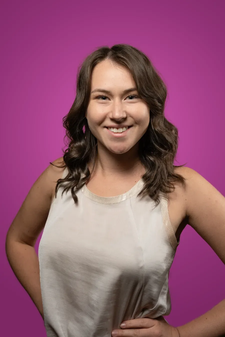 A smiling woman with wavy hair against a pink background.