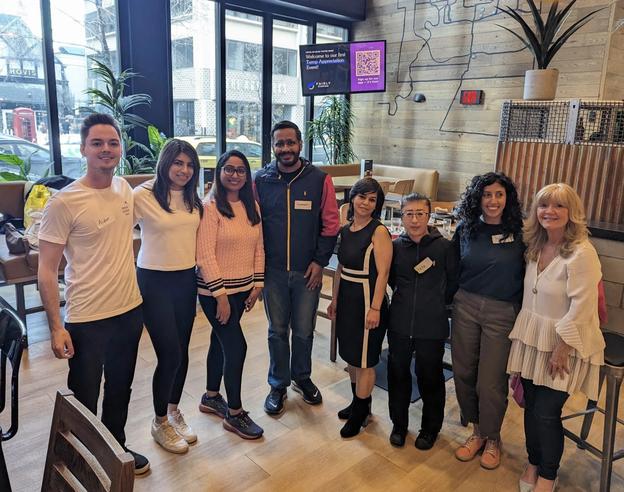 A group photo of eight people in a café setting.