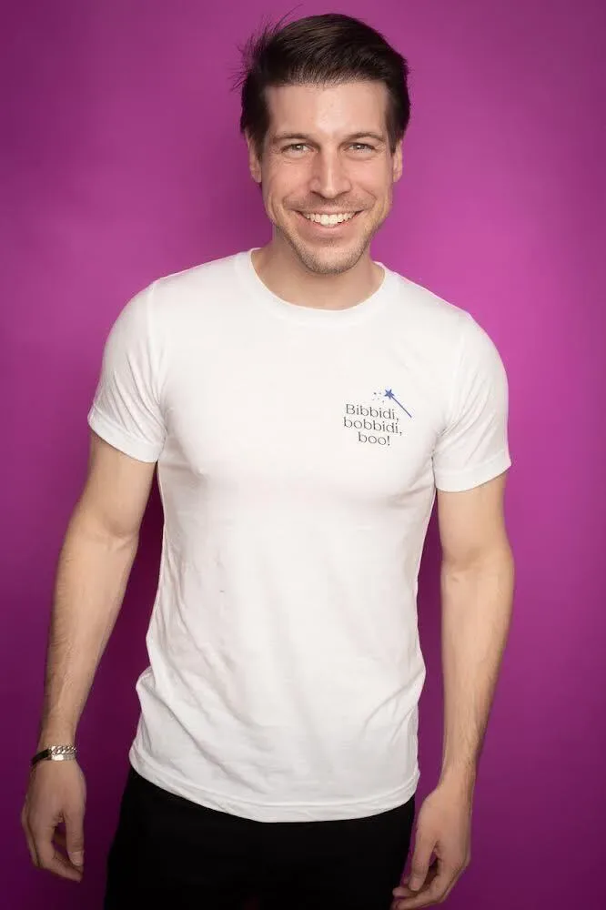 A man smiling in a white t-shirt against a pink background.
