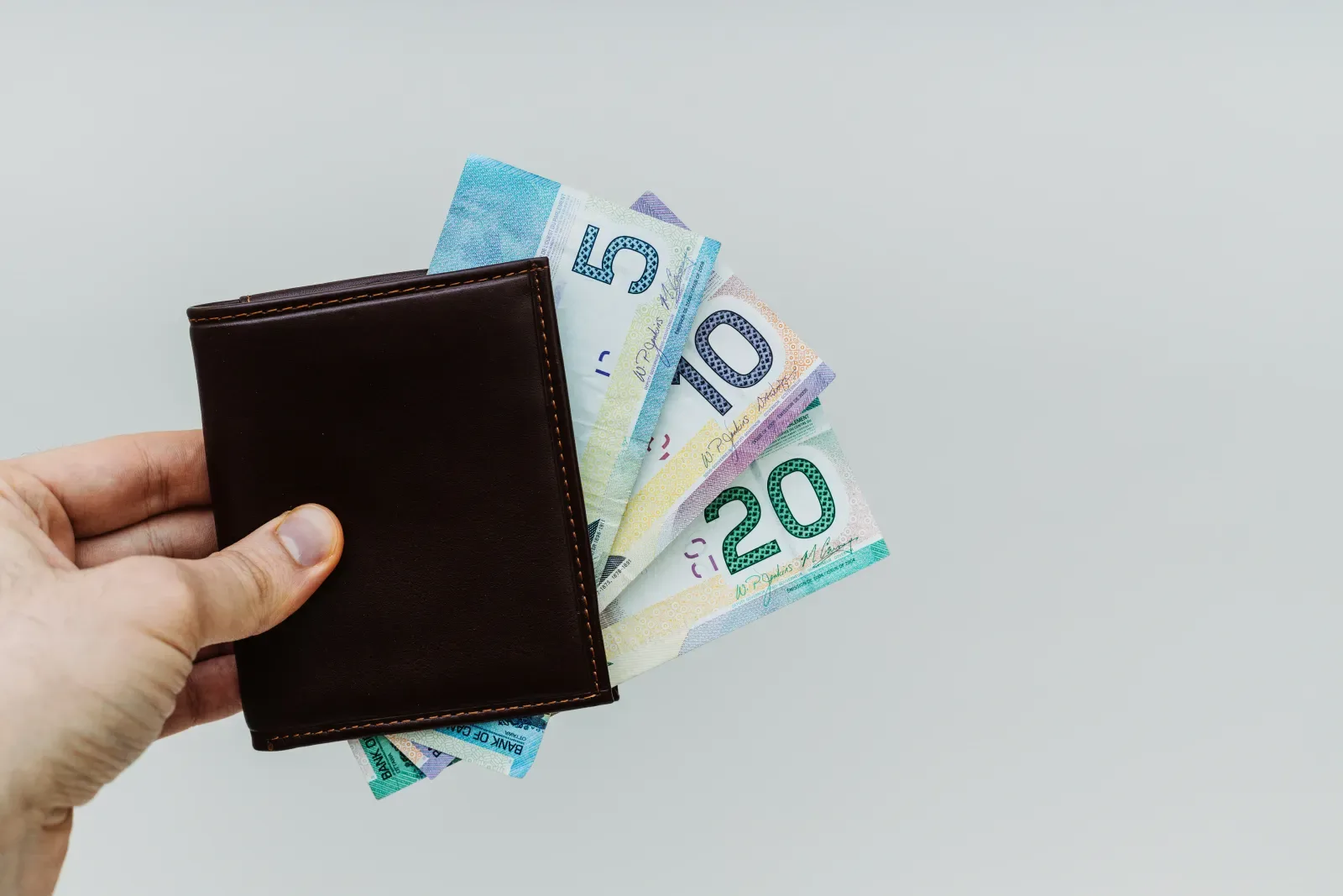 Hand holding a brown wallet with colorful money.