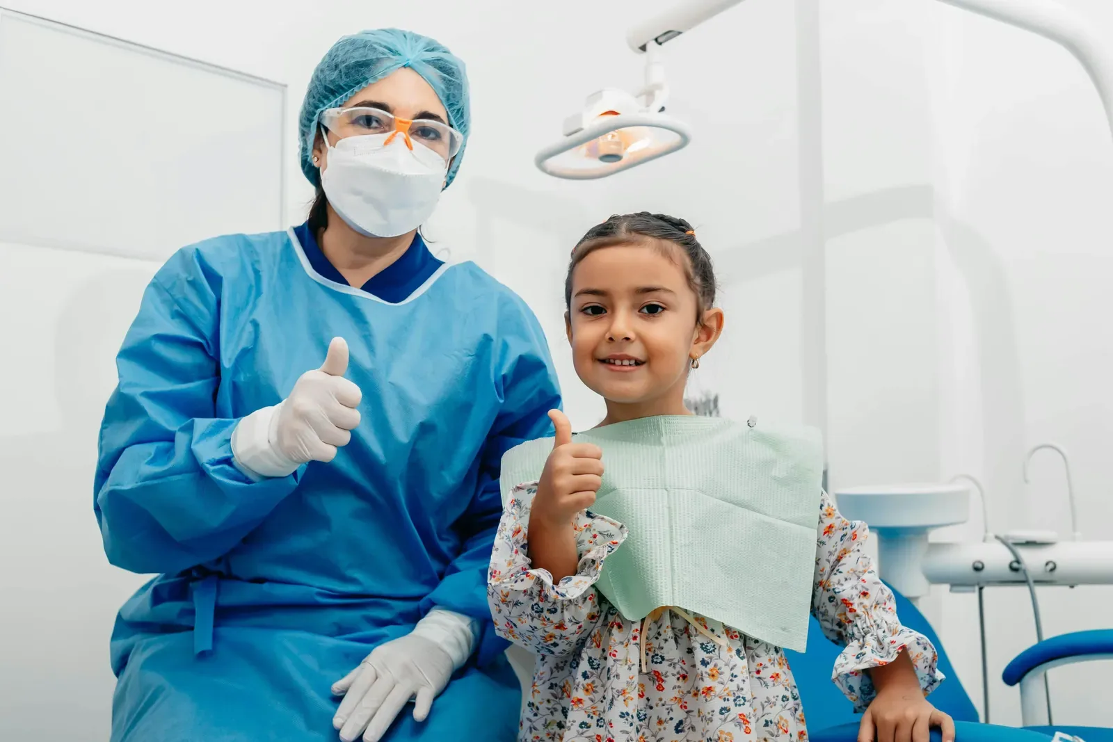 Dental professional and young girl giving thumbs up in clinic.