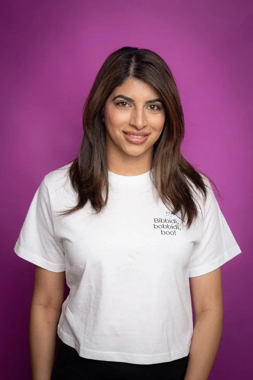 A woman with long hair wearing a white shirt against a purple background.