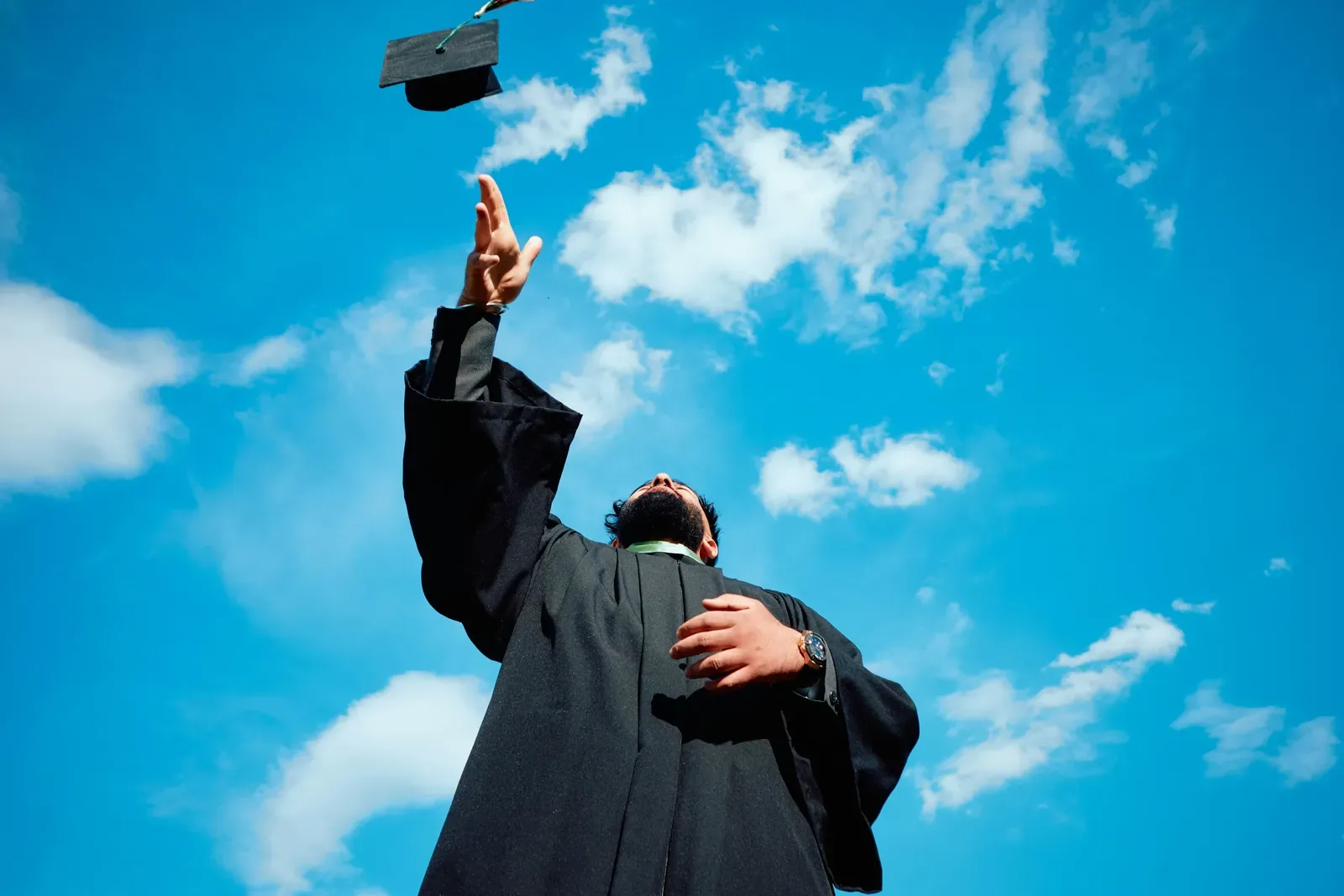 A man in a graduation gown throwing his cap into the sky.