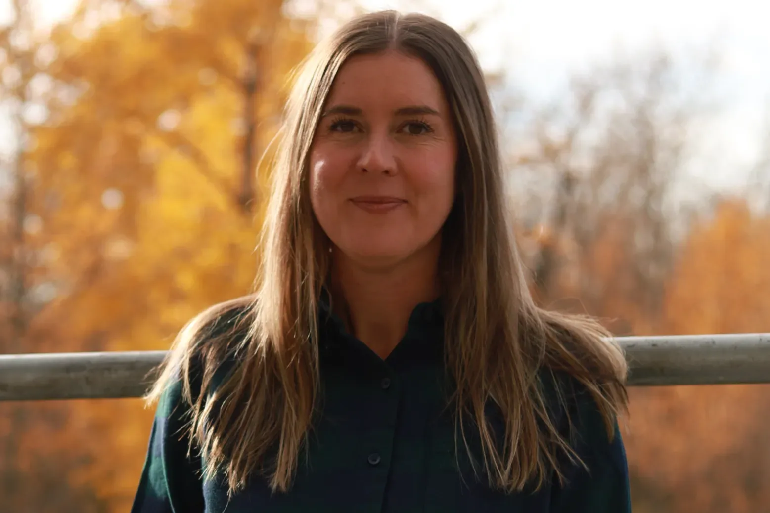 A woman with long hair smiling in an autumn setting.