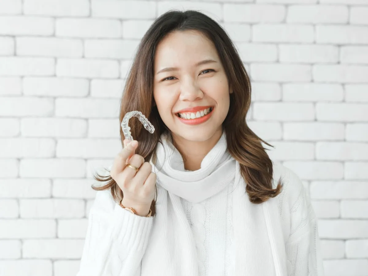 Smiling woman holding a clear Invisalign aligner.