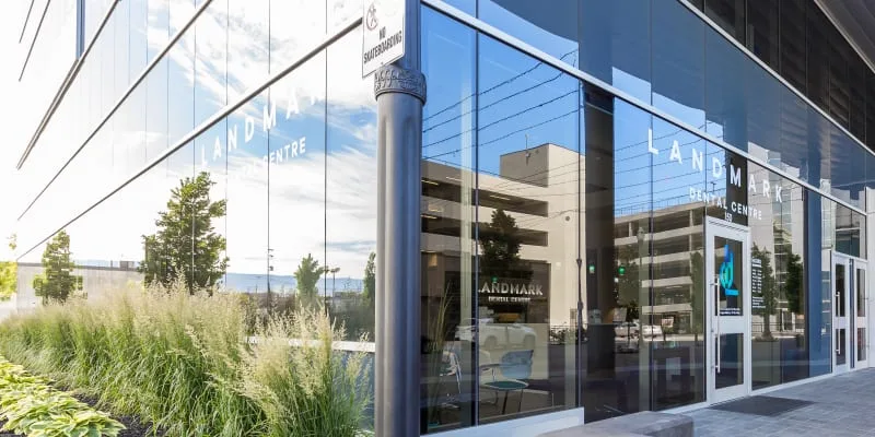 Exterior view of Landmark Dental Centre with glass windows and plants.