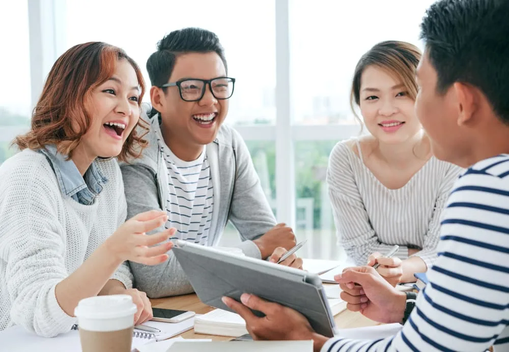 A group of four young adults smiling and discussing at a table.