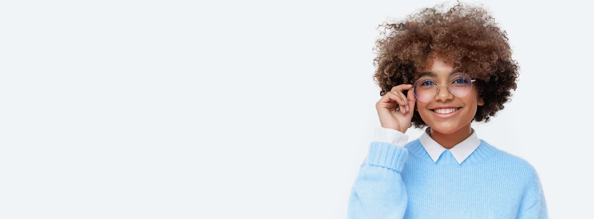 A smiling young woman with glasses and curly hair in a blue sweater.