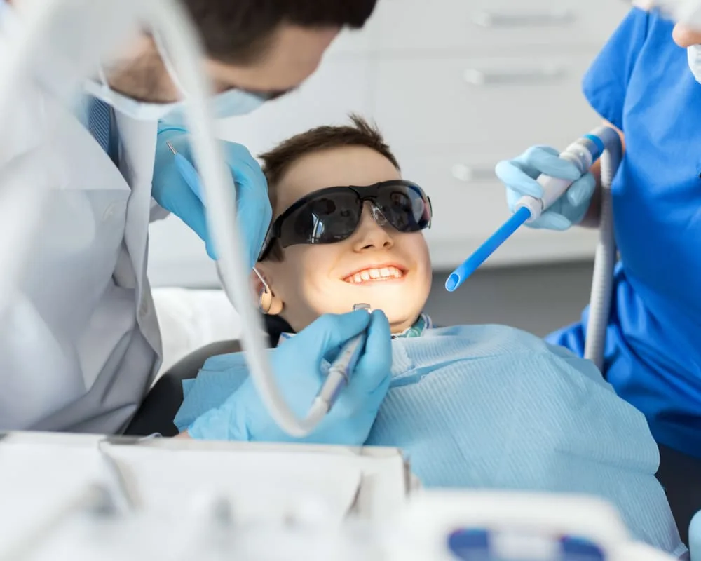 A young boy smiling in a dental chair with professionals.