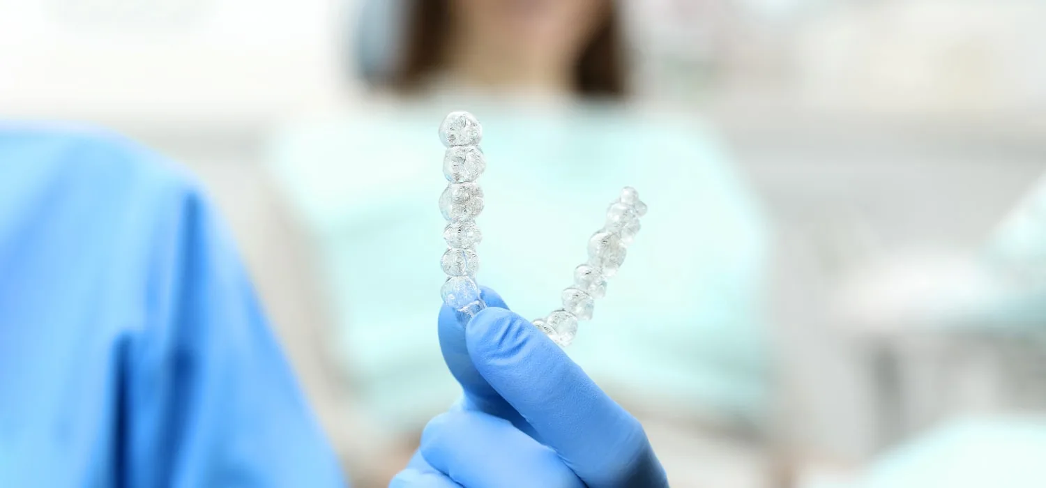 A gloved hand holding two sets of clear dental aligners.
