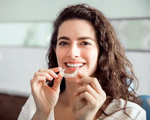 A smiling woman holding a dental aligner in a dental office.