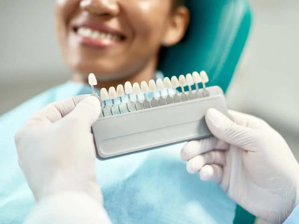 A dental professional shows a shade guide to a smiling patient.