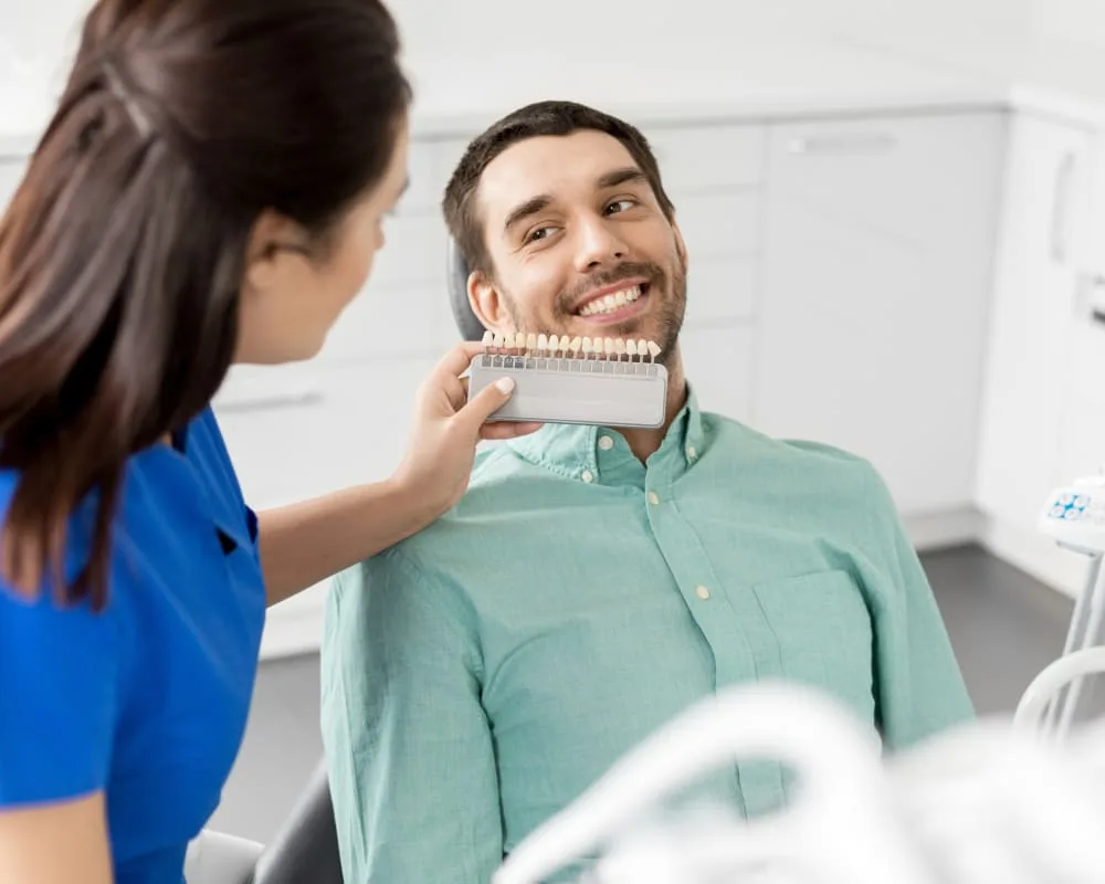 A dental professional comparing shade guide with a smiling patient.