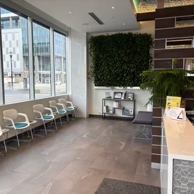 A modern dental office waiting area with white chairs and green plants.
