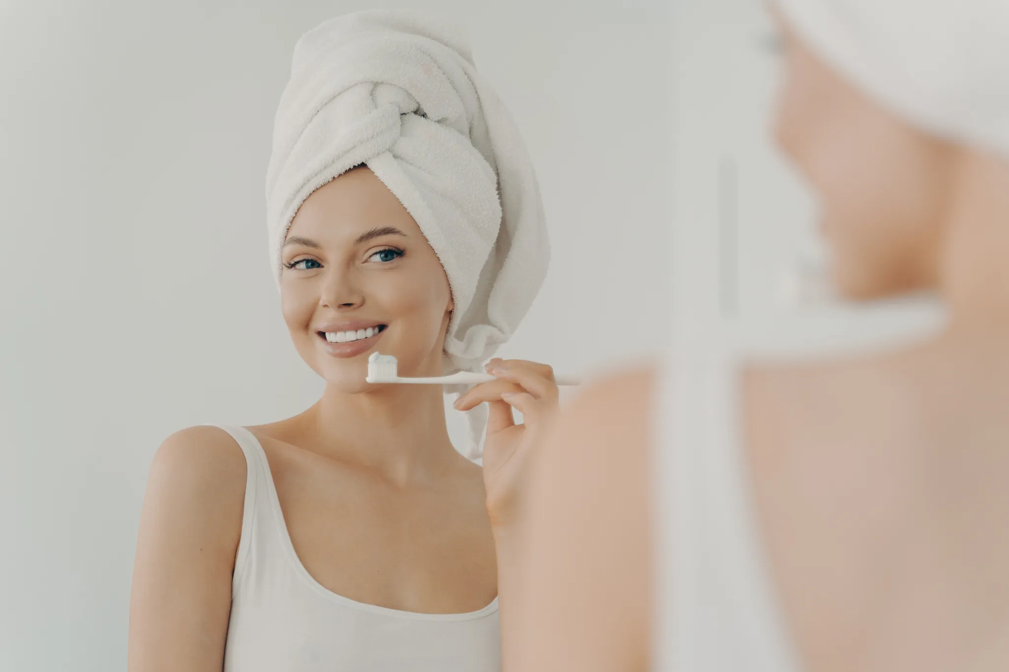 A woman smiling while brushing her teeth in a bathroom.