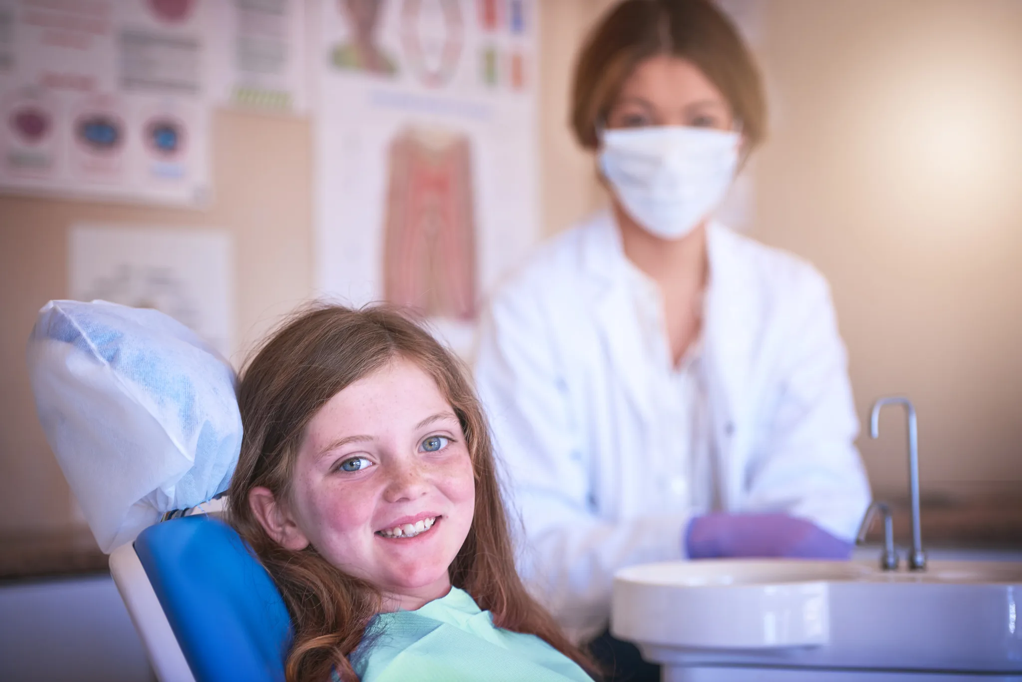 A young girl smiling in a dental chair with a dentist nearby.