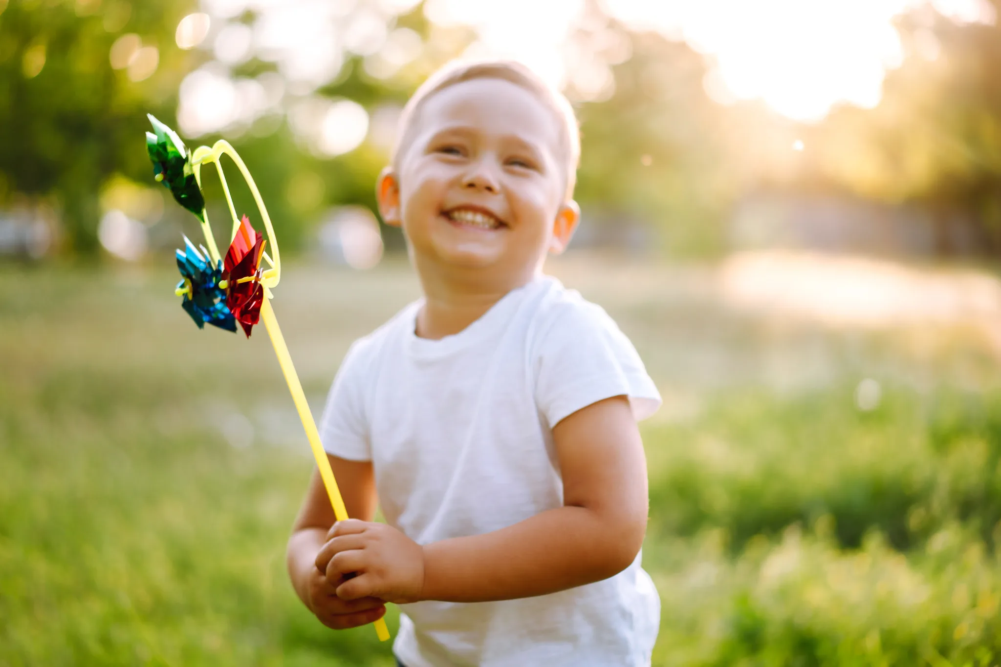 Smiling child holding a colorful toy in a sunny park