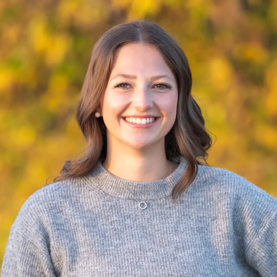 A smiling woman in a gray sweater outdoors.