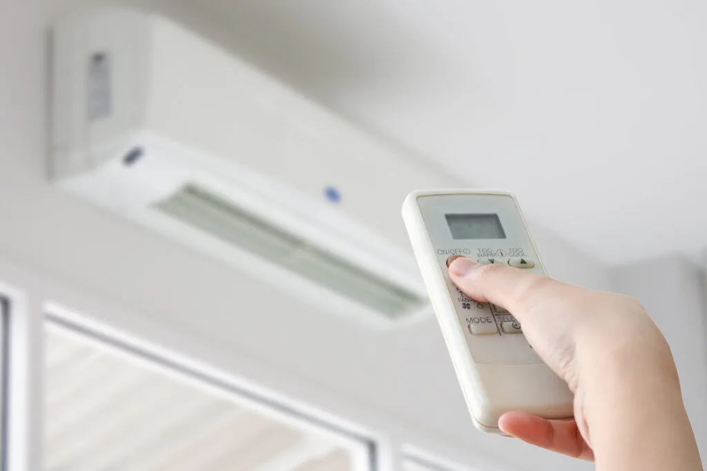 Hand holding a remote control for air conditioning.