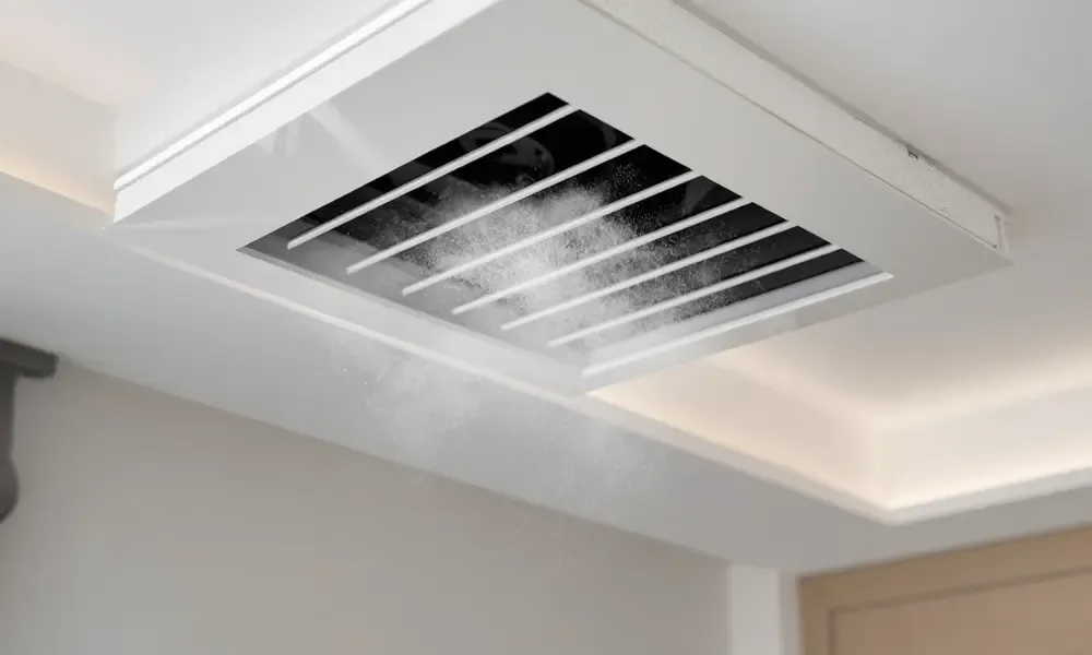 Ceiling HVAC vent releasing dust particles in a modern interior.