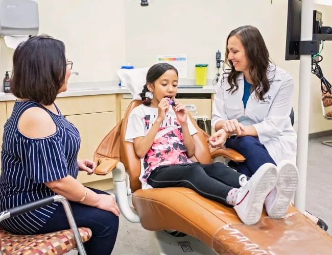 A young girl with a dentist and parent in a dental office.