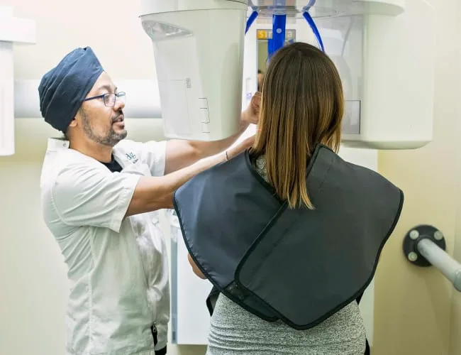 A dentist assists a patient with dental imaging equipment.