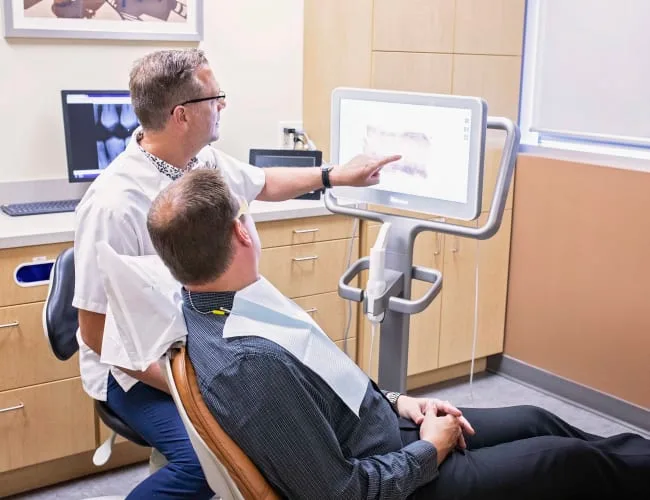A dentist assists a patient with digital imaging in a dental office.