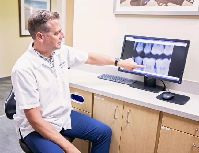 A dentist pointing at a dental x-ray on a computer.