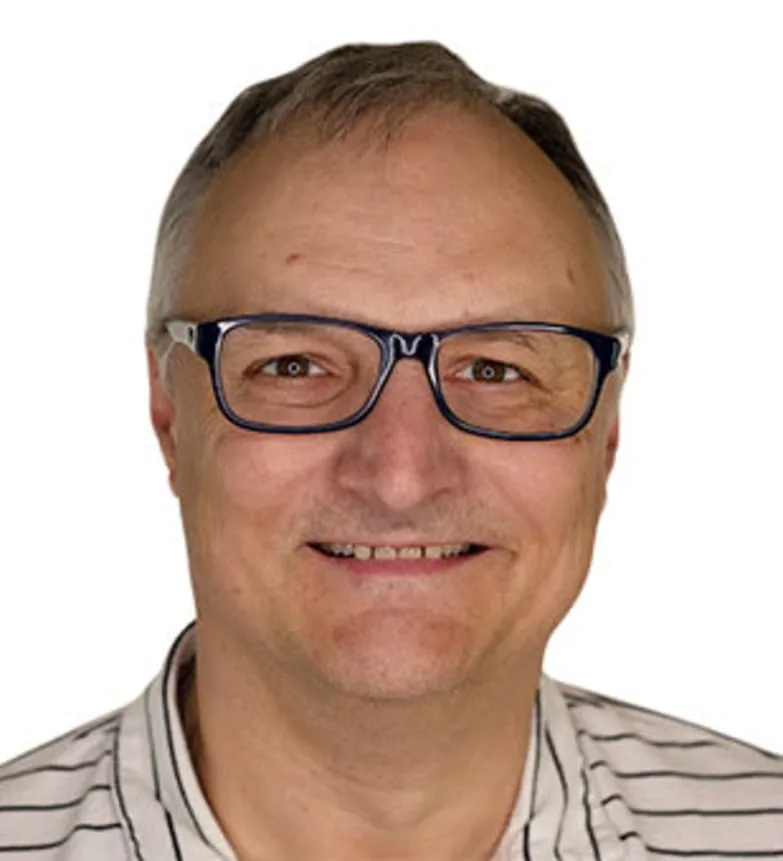A smiling man in glasses with gray hair and a striped shirt.