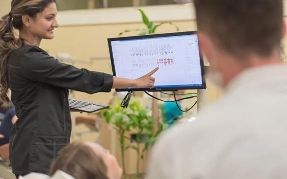 A dental hygienist shows a patient information on a monitor.