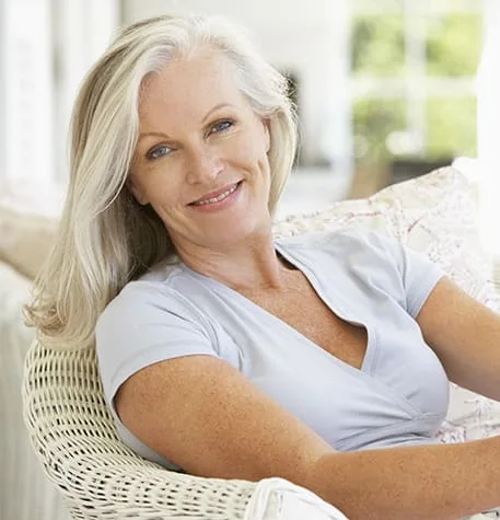 Smiling older woman sitting in a wicker chair.