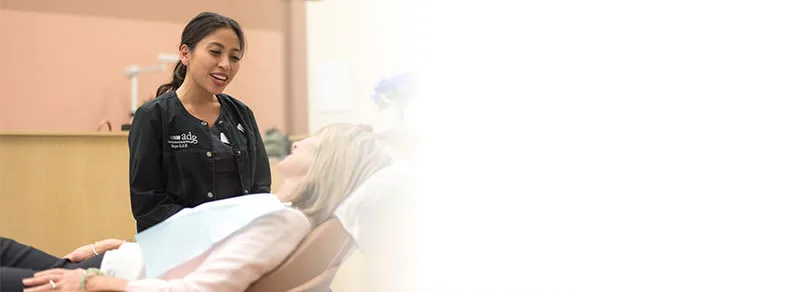 A dental hygienist converses with a patient in a dental chair.