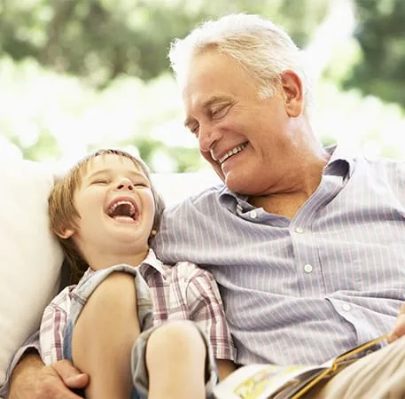 A grandfather and grandson laughing together on a couch.