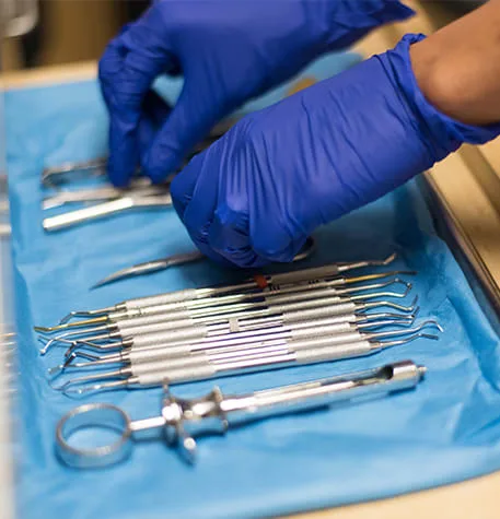 Dental instruments arranged on a blue tray by gloved hands.